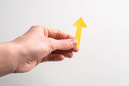 Hand holding a yellow paper arrow pointing up on white backgroundの写真素材