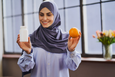 A bottle of pills and an orange in Arabian womans handsの写真素材
