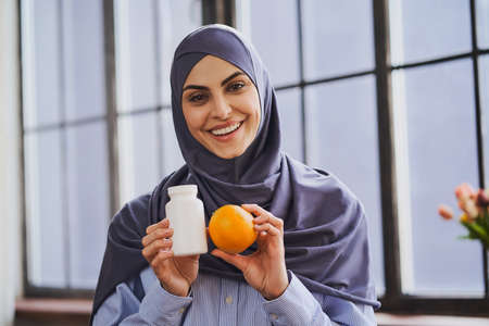 Charming Arabian woman holding a bottle of pills and an orangeの写真素材