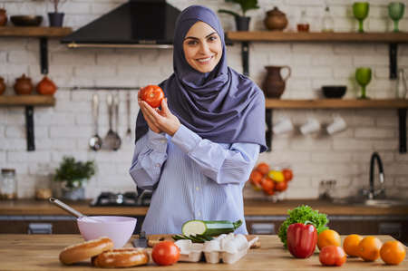 Cheerful Muslim woman showing a tomato and talking about ingredientsの写真素材