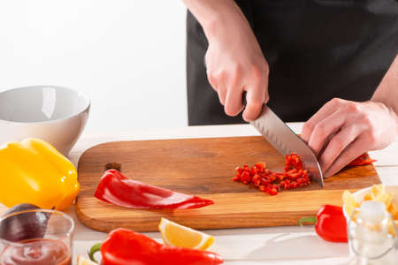 Hands cutting red pepper into fine dice on a wooden boardの写真素材