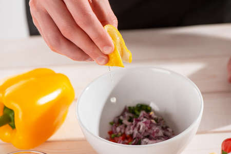 Hand squeezing lemon juice into a bowl with freshly cut ingredientsの写真素材