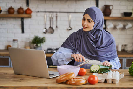 Arabian woman cutting ingredients and watching a tutorial on her laptopの写真素材