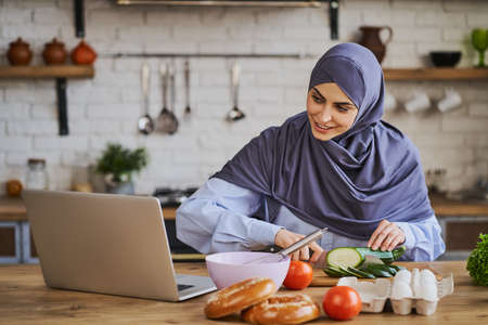 Muslim housewife cooking a meal and watching a movie on a laptopの写真素材