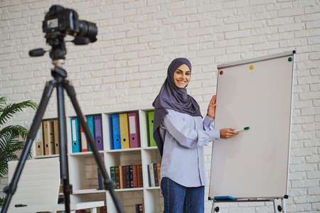 Arabian female coach making a video as she showing something on a whiteboardの写真素材