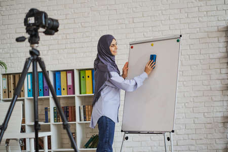 Muslim teacher cleaning the whiteboard while making a videoの写真素材