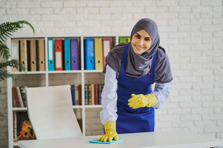 Smiling Arabian woman cleaning a table in the officeの写真素材
