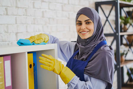 Portrait of a gorgeous Muslim woman cleaning shelves with booksの写真素材
