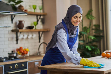 Joyful Muslim woman cleaning a table in the kitchenの写真素材