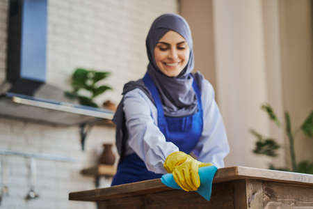Arabian woman cleaning a kitchen table, using a rag and wearing glovesの写真素材