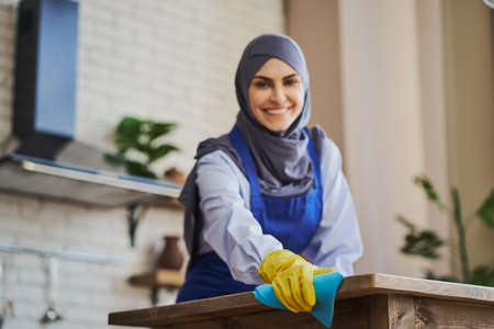 Muslim woman wearing apron and gloves while cleaning a houseの写真素材