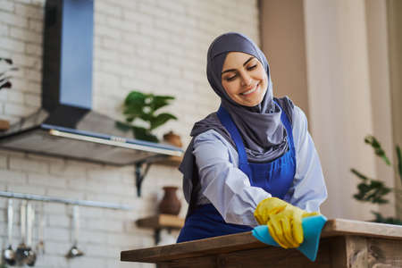 Cheerful Arabian woman wiping the dust off the tableの写真素材