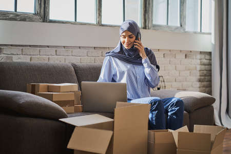 Muslim woman talking on the phone and looking at a laptopの写真素材