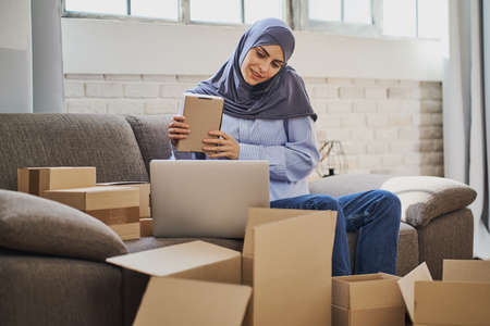 Muslim business woman talking on the phone and packaging orders from her shopの写真素材