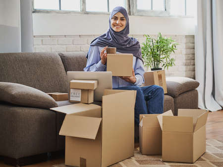Arabian woman sitting on the couch with a laptop and packing ordersの写真素材