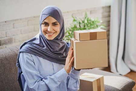 Pretty Arabian woman holding few carboard boxes and giving a broad smileの写真素材