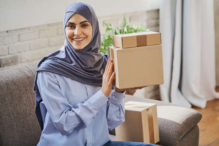 Arabian woman holding cardboard boxes and giving a smile to the cameraの写真素材
