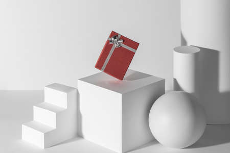 Red gift box with silver ribbon among white 3d shapesの写真素材