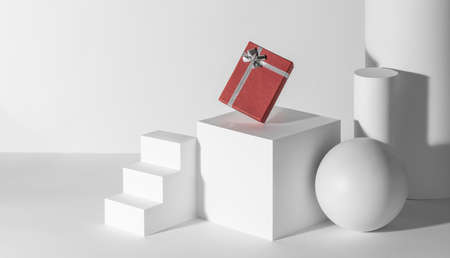 Red gift box with silver ribbon among white 3d shapesの写真素材