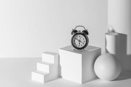 Black alarm clock on white 3d paper shapes with copy space