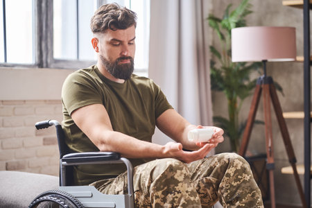 Depressed ex-serviceman sitting in a wheelchair and taking prescribed pillsの写真素材
