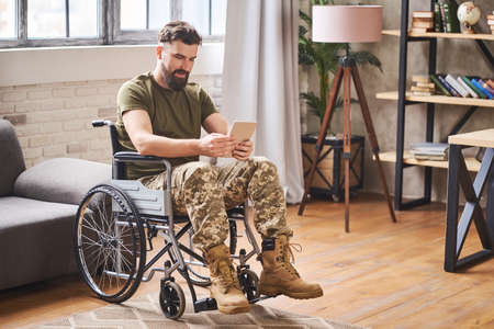 Disabled handsome military man sitting in a wheelchair and using a tabletの写真素材