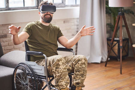 Joyful ex-serviceman sitting in a wheelchair and wearing a VR headsetの写真素材
