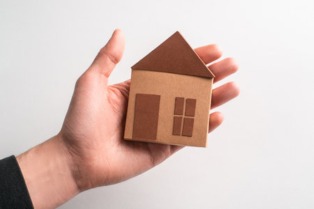Cute brown paper house laying on a hand on white backgroundの写真素材
