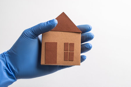 Hand in glove holding a paper house on white backgroundの写真素材