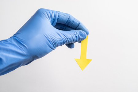 Hand in glove holding a yellow paper arrow pointing downの写真素材