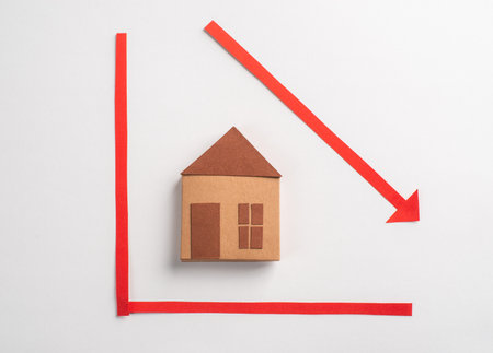 Paper house toy on a chart with red arrow pointing downの写真素材