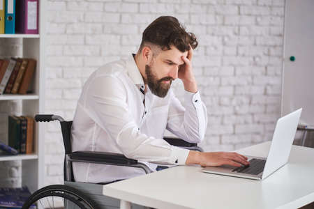Businessman sitting in a wheelchair and working with a laptopの写真素材