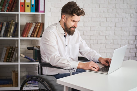 Chief sitting in a wheelchair and working on a laptopの写真素材