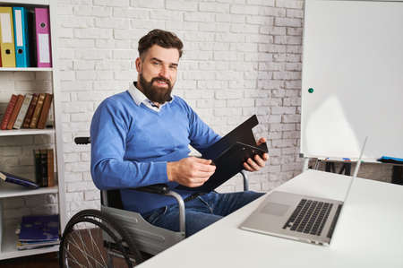 Handsome businessman sitting in a wheelchair and holding a clipboardの写真素材
