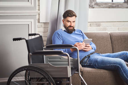 Portrait of a man with disability laying on a couch and using a tablet computerの写真素材