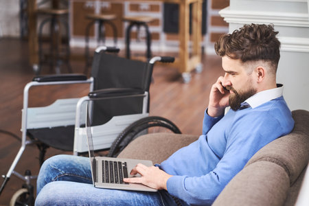 Successful businessman with disability sitting on a couch, working on a laptopの写真素材