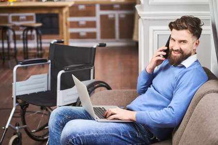 Cheerful disabled businessman sitting on a couch, working on a laptopの写真素材