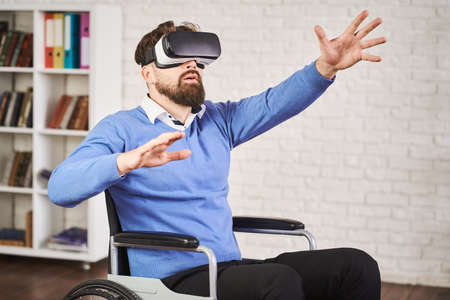Portrait of a disabled man sitting in a wheelchair and using a VR headsetの写真素材