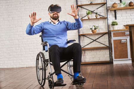 Joyful man sitting on a wheelchair and wearing a VR headsetの写真素材