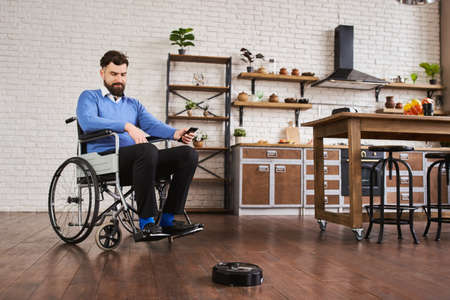 Man sitting in a wheelchair and using a robotic vacuum connected to his phoneの写真素材