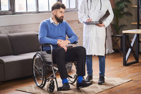 Man with disability listening to a doctor in his homeの写真素材