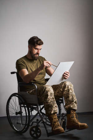 Young military man sitting in a wheelchair and painting on a canvasの写真素材