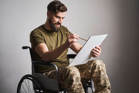 Military man sitting in a wheelchair and painting a picture with a brushの写真素材