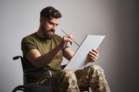 Ex-serviceman sitting in a wheelchair and painting a picture on a canvasの写真素材