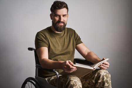 Happy military man sitting in a wheelchair and watching album photosの写真素材