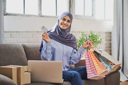 Happy Musim woman holding a credit card and a bunch of gift bagsの写真素材