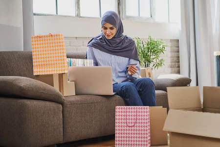 Joyful Arabian woman sitting on a couch and using a laptop to buy giftsの写真素材