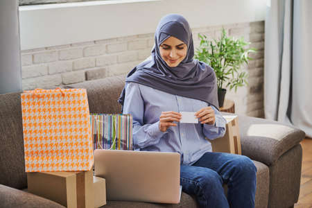Pretty Muslim woman sitting on a couch and buying something onlineの写真素材