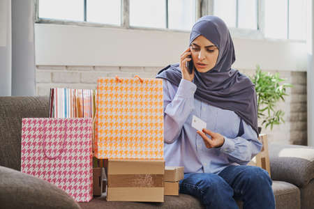 Serious Muslim woman holding a credit card and talking on the phoneの写真素材