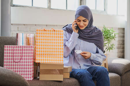 Glad Muslim woman talking on the phone and holding a plastic cardの写真素材
